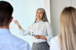 © insta_photos - Mature happy smiling Asian corporation female executive ceo presenting project research results to interns colleagues business partners team standing pointing at board room in modern office.