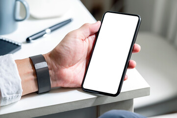 Wall Mural - cropped shot of man hand holding blank screen smartphone while sitting at the table.