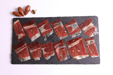 Wall Mural - Portion of 100% acorn-fed Iberian ham Dehesa de Extremadura on a slate plate decorated with acorns and a white background viewed from above