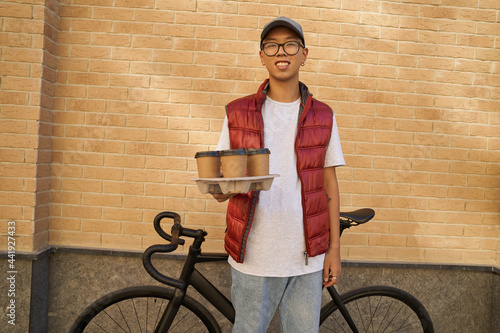 Young cheerful asian male courier holding four cups of coffee an
