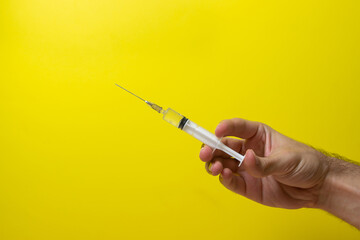 Hand holds a syringe on a yellow background. Vaccination and health protection concept