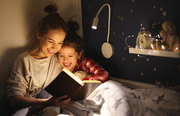 Happy mother and daughter reading book together on bed