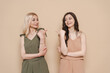 © diignat - Blonde mother and brunette adult daughter wearing identical clothes, different colors, posing over beige background pointing fingers to each other
