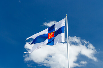 Wall Mural - State flag of Finland with national coat of arms against blue sky on the wind