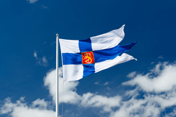 Wall Mural - State flag of Finland with national coat of arms against blue sky on the wind