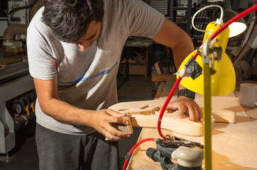 Latin man sanding the body of a guitar by hand. Concept of making a handmade guitar.