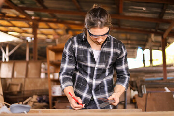 Wall Mural - Caucasian carpenter man is using solid square measuring to scale the plank of wood in his own garage style workshop for hobby