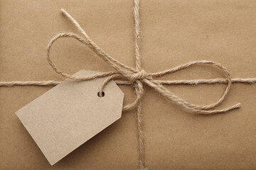 Parcel wrapped in kraft paper with tag as background, closeup