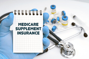 There is a stethoscope on the table, the doctor holds a notebook in his hand with the inscription - MEDICARE SUPPLEMENT