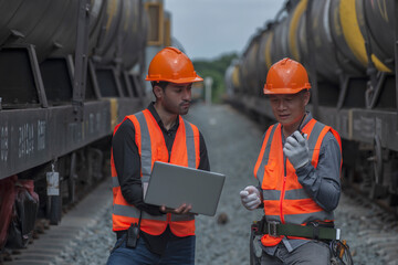 workers at work. two engineer co-work on laptop between oil tank bogie in station.