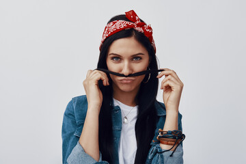 Wall Mural - Attractive young woman in bandana making a face while standing against grey background