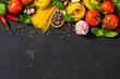 © kucherav - Italian food ingredients with pasta, tomatoes, pepper, garlic and parsley on dark background with copy space, top view