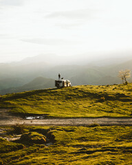 Poster - Back view of a Spanish man and a dog admiring nature while standing on a camper van parked on a hill