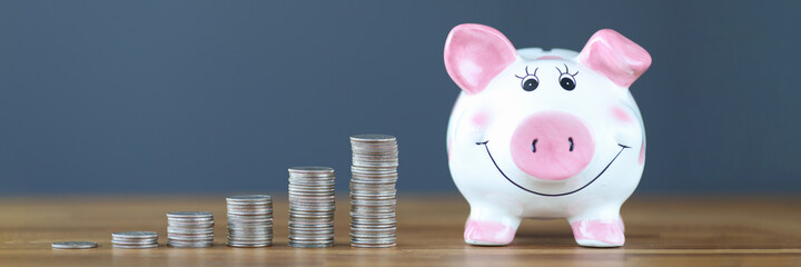 Wall Mural - Pink piggy bank standing on table near heaps of coins