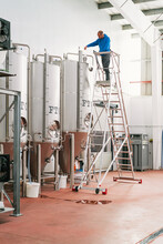 Brewer On Ladder Filling Fermentation Reservoir In Beer Factory