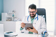 © ADDICTIVE STOCK - Smiling physician with tablet during video call in clinic