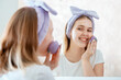 Woman washes her face with natural sponge and soap scrub cosmetic foam in bathroom portrait reflection in mirror. Teenage girl blonde do self care morning routine. Scin care cosmetic life style