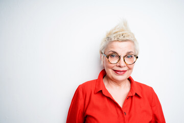 Cute elderly woman in a red shirt with blond short hair wearing glasses looking at the camera