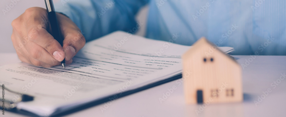 Real estate agent holding home and signing contract about agreement of real property on desk, house broker and planning investment, businessman writing on document form rent house, business concept. - obrazy, fototapety, plakaty 