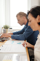 Canvas Print - Serious business people working on project at office desk, typing on laptop and signing documents