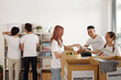 © DragonImages - Group of young people working in community donation center, unpacking boxes and putting groceries and clothes on shelves