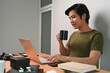 © Prathankarnpap - Smiling casual man holding coffee cup and browsing internet with laptop at home.