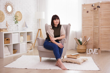 Wall Mural - Brunette woman sitting on armchair in living room.