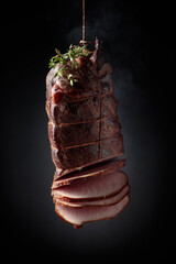 Wall Mural - Sliced smoked gammon with thyme branches on a black background.