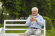 © Studio Romantic - Happy senior citizen looking at screen of his mobile phone. Cheerful active white haired old man using smartphone sitting on park bench against blurred copy space background of summer park greenery