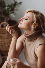 Young Beautiful Woman Holds A Bottle Of Perfume In Her Hands And Inhales While Enjoying The Fragrance From Her Wrist. Soft Selective Focus.