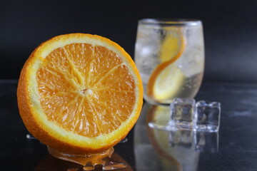 lemonade with orange and ice in a glass on a black background next to lies ice and orange. Summer drink on a black background