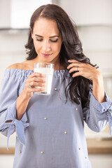 Wall Mural - Woman smiles and looks into her glass of milk in the hand standing in the kitchen