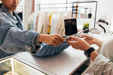 Female buyer giving clothes to unrecognizable clerk for checkout