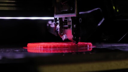 Three dimensional printer making red flat physical plastic 3D model at modern futuristic exhibition - close up. Additive technology, equipment, prototype, manufacturing and production concept