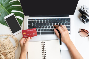 Wall Mural - Flat lay of woman hand typing on keyboard while holding credit card with travel accessories and mobile phone on desk. Summer, holiday, work and planning traveling concepts. Top view and copy space