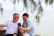 © sutthichai - Happy Asian senior father using smartphone with his son
