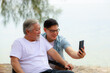 © sutthichai - Happy Asian senior father using smartphone with his son