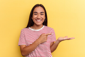 Wall Mural - Young mixed race woman isolated on yellow background excited holding a copy space on palm.