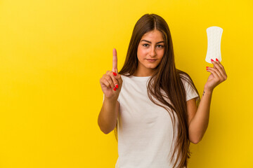 Young caucasian woman holding a compress isolated on yellow background showing number one with finger.