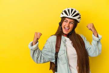 Wall Mural - Young student caucasian woman wearing a bike helmet isolated on yellow background raising fist after a victory, winner concept.