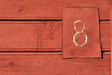 Fragment Of The Wall Of An Old Rural Village House. The Boards Are Covered With Red Paint And There Is A Hand-made Sign With The Number 8. Background. Texture. 