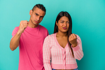 Young latin couple isolated on blue background showing fist to camera, aggressive facial expression.