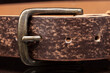 Brown leather belt with scuffs and a metal buckle on a dark background.
