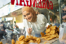 A Beautiful Girl In A Veil With Finger Pointing While Choosing Fried Food On A Roadside Cart. Gorengan Is Indonesian Word Mean Fried Snack