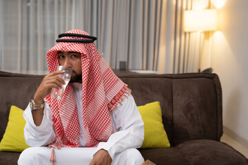 Wall Mural - an Arab young man drinking water using a glass while sitting indoors