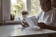 © Мария Чичина - Elderly woman sitting at table in kitchen at home holds domestic bills, feels concerned forgot to pay or debt formed. Middle aged 80s retired woman