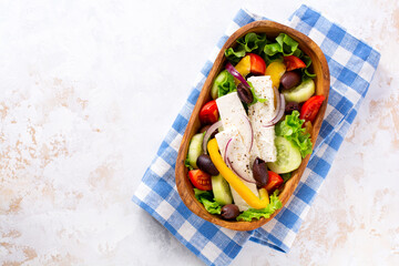 Fresh greek salad with tomato, cucumber, bel pepper, olives and feta cheese on wooden plate. Traditional Greek dish. Healthy food, top view