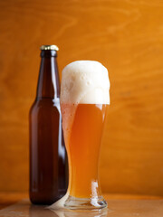 Wall Mural - A tall glass of a pint of beer on a wooden table, a beer bottle. Unfiltered traditional wheat beer