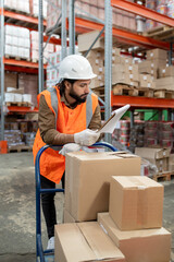 Warehouse engineer with cart looking through list of goods