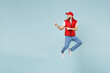 © ViDi Studio - Full size body length side view delivery guy employee man in red cap white T-shirt vest uniform work dealer courier jump run go walk isolated on pastel blue color background studio. Service concept